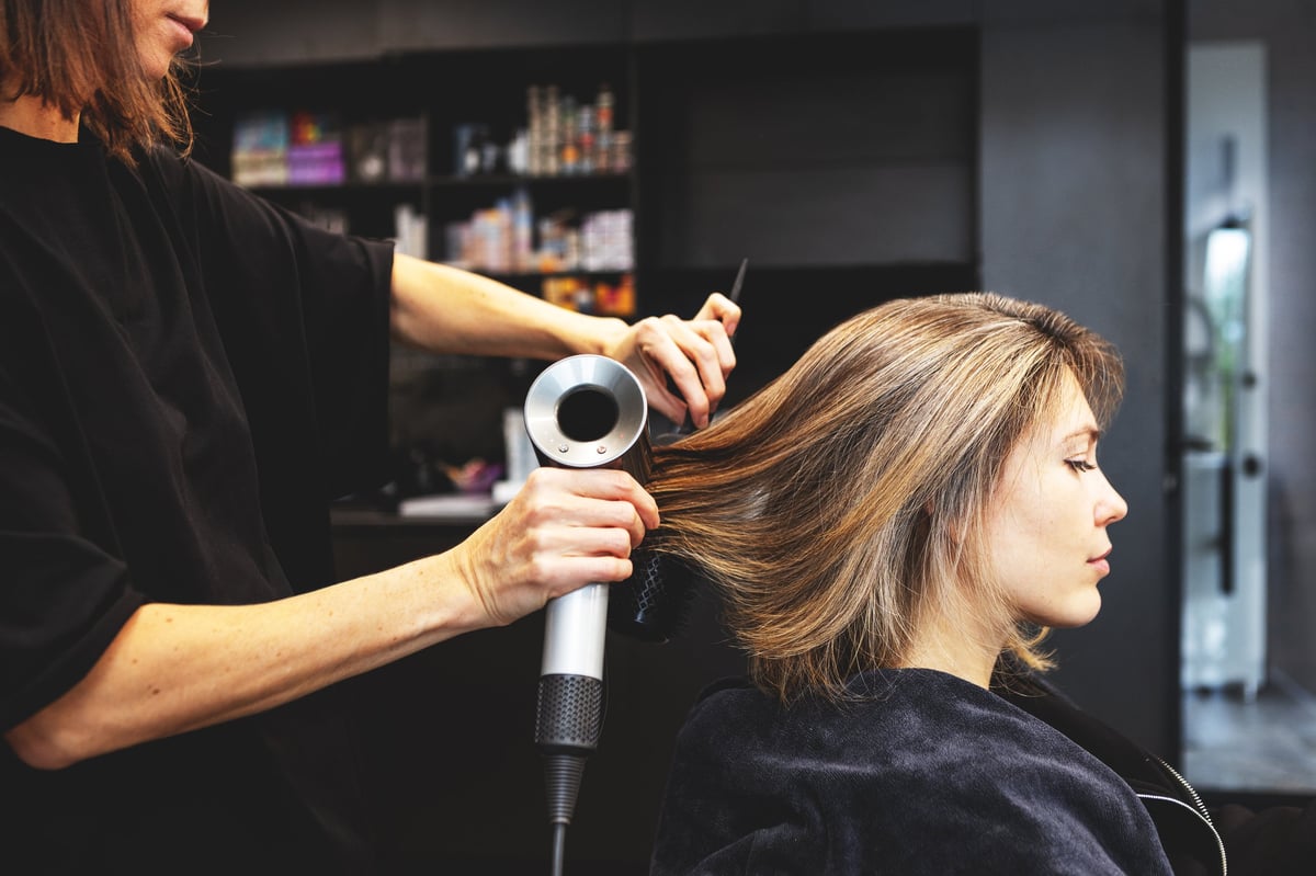 A stylist blow-drying and shaping a client's hair at Hair by Trish